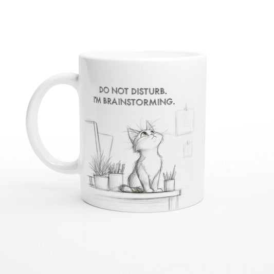 White mug with a pencil-sketch cat on a desk, plants nearby, and the slogan DO NOT DISTURB. I'M BRAINSTORMING.